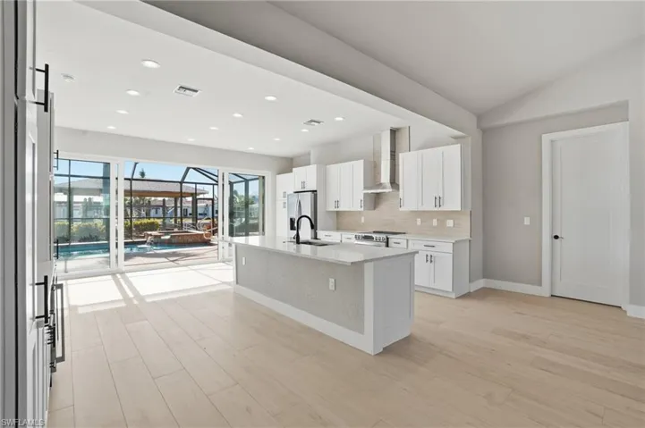 Kitchen with a sunroom, an island with sink, tasteful backsplash, white cabinetry, and light wood-type flooring - Virtually Edited Image