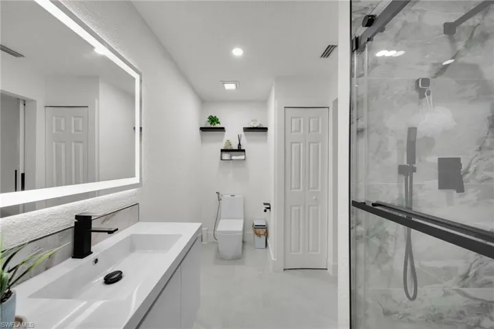 Contemporary bathroom featuring an integrated sink vanity with a black faucet, an illuminated mirror, and a frameless glass shower enclosure