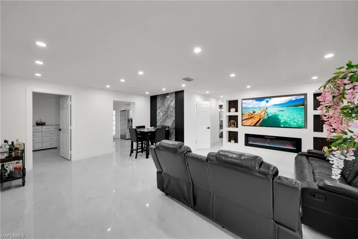 Spacious living area featuring light-toned tile flooring, recessed lighting, and a built-in media wall