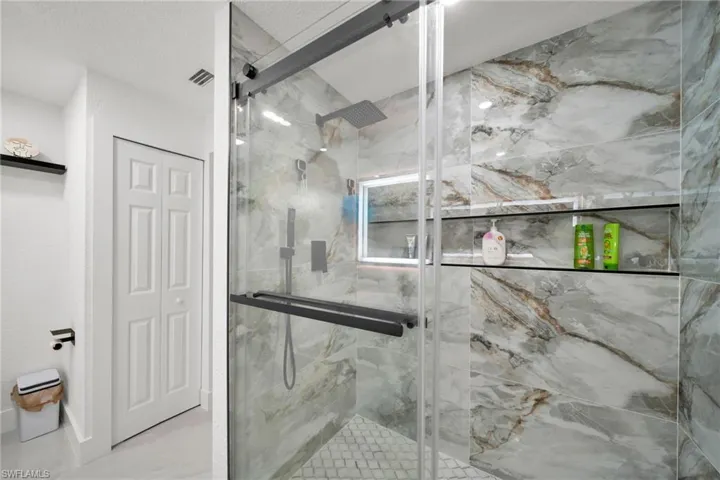 Walk-in shower featuring large format veined wall tiles, a built-in recessed shelf with integrated lighting, and dark-framed glass enclosure