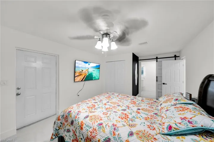 Bright room featuring a white paneled door with dual door knobs, a ceiling fan with light fixture, and a sliding barn door entry