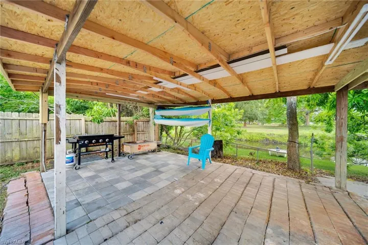 Covered outdoor patio featuring a combination of paver and wood-finish flooring, exposed wood beam ceiling, and a fenced perimeter
