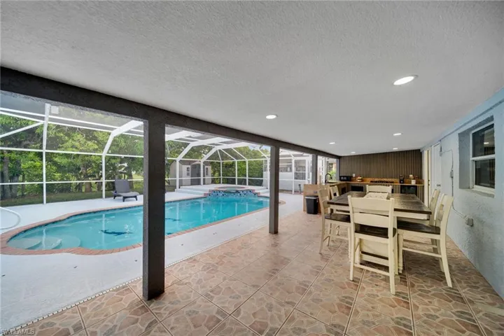 Screened patio with a built-in outdoor kitchen, patterned tile flooring, and recessed lighting