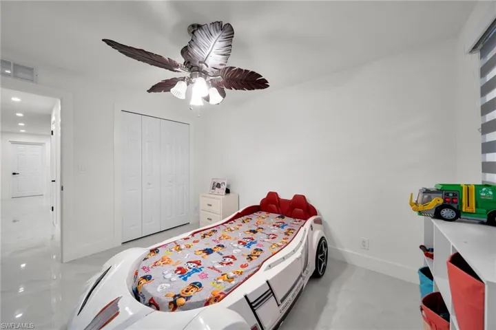 Room featuring a ceiling fan with decorative leaf-shaped blades, white bi-fold closet doors, and recessed lighting in the hallway