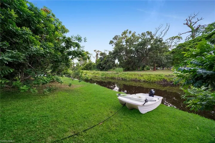 Expansive green lawn bordering a tranquil water feature, surrounded by mature trees