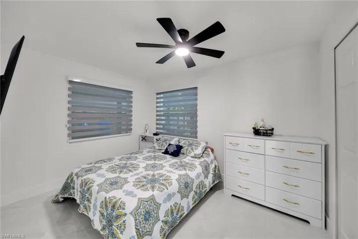 Room featuring a modern ceiling fan, two windows with horizontal blinds, and light-toned flooring