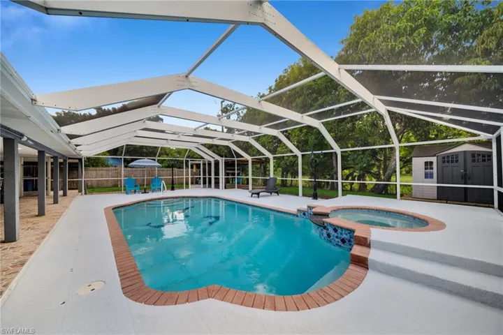 Screened outdoor living area featuring a swimming pool, integrated hot tub, and a spacious pool deck