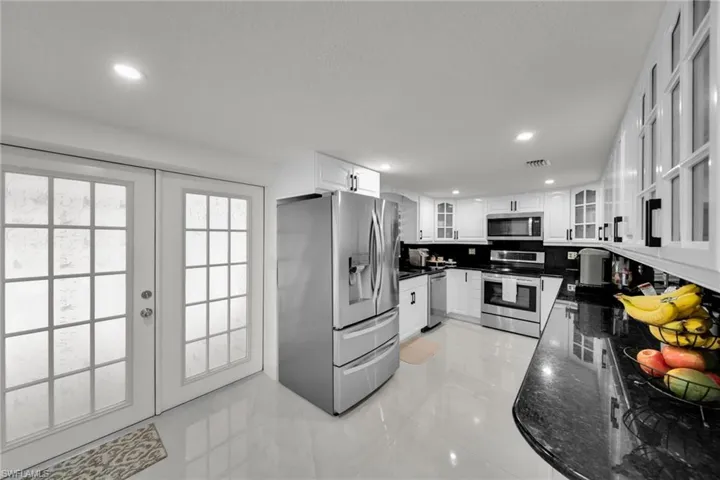Kitchen featuring a full suite of stainless steel appliances, white cabinetry with black hardware, dark countertops, recessed lighting, and white French doors