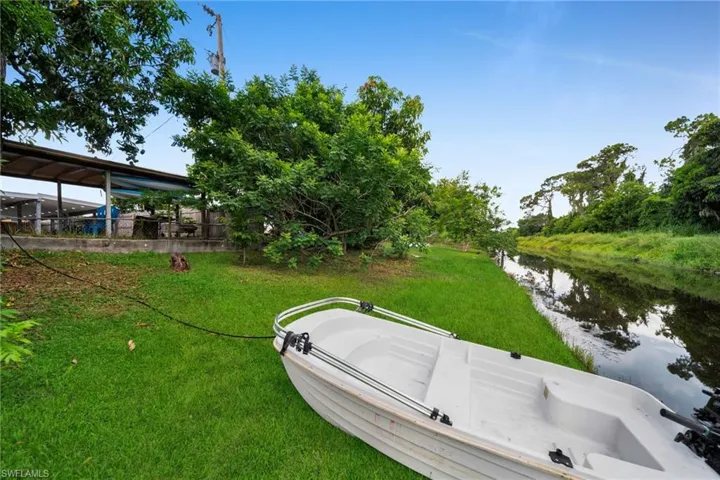Waterfront property featuring a grassy bank, mature trees, and a covered patio structure