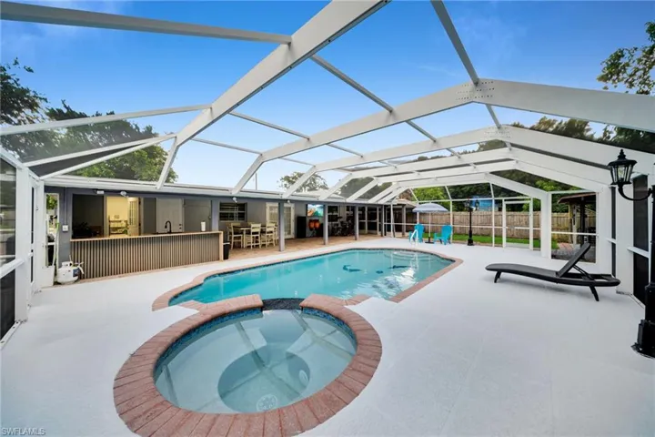 Screened enclosure featuring a freeform swimming pool with integrated spa, a dedicated outdoor kitchen area with a built-in countertop, and ample paved deck space