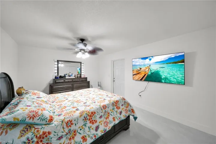 Spacious bedroom featuring light-toned flooring, a ceiling fan with integrated lighting, and a wall-mounted television