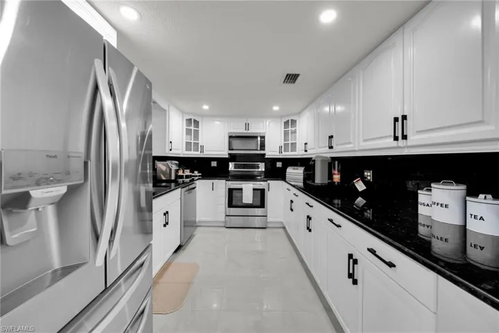 Galley kitchen featuring white cabinetry with black hardware, dark countertops, and stainless steel appliances