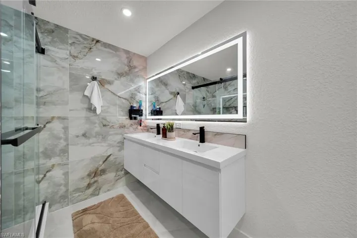Modern bathroom featuring a dual vanity with rectangular sinks, black matte fixtures, and an illuminated mirror