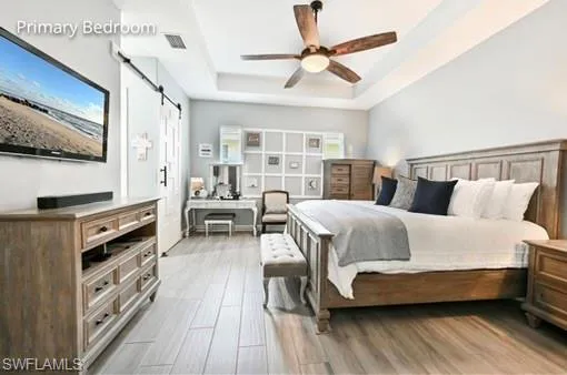Bedroom with a barn door, a raised ceiling, hardwood / wood-style floors, and ceiling fan