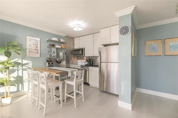 Kitchen featuring decorative backsplash, stainless steel appliances, light hardwood / wood-style floors, crown molding, and white cabinets