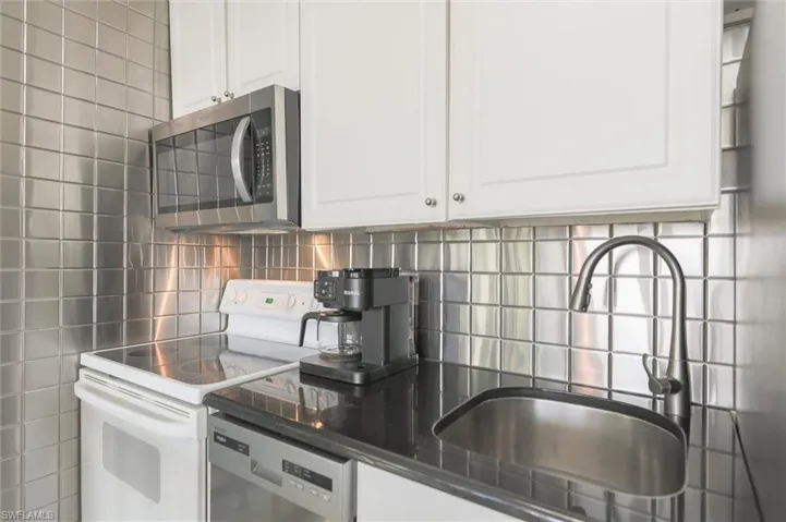 Kitchen with decorative backsplash, sink, white range with electric cooktop, dishwashing machine, and white cabinets