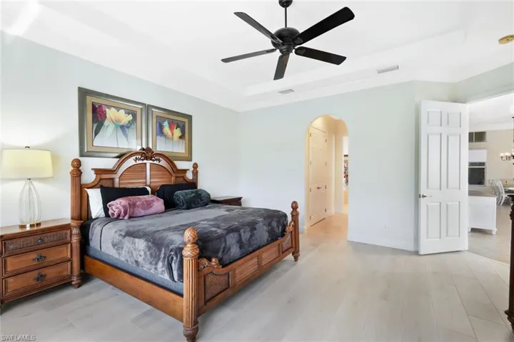 Bedroom with a raised ceiling, light wood-type flooring, a ceiling fan, and arched walkways