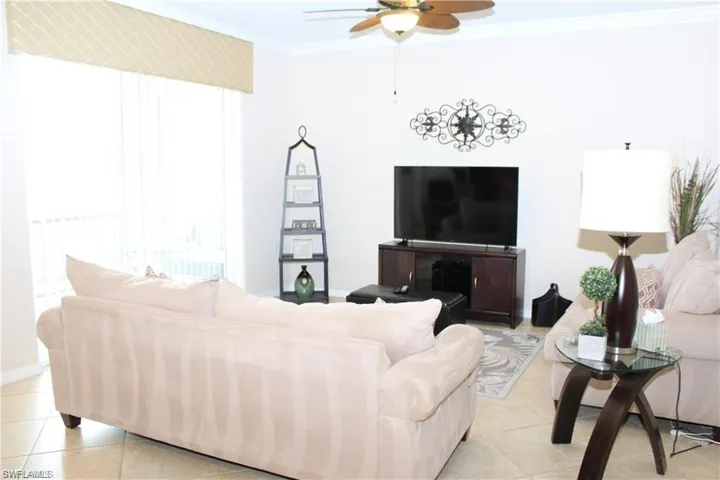 Living room with light tile patterned flooring, ceiling fan, baseboards, and crown molding