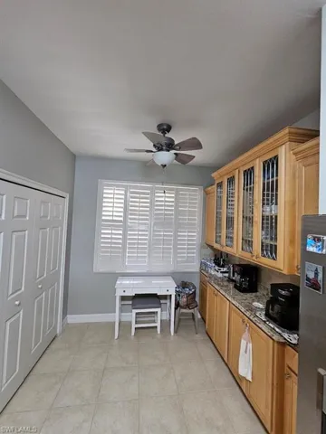 Kitchen featuring glass insert cabinets, a ceiling fan, light tile patterned flooring, dark stone countertops, and freestanding refrigerator