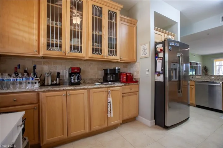 Kitchen featuring appliances with stainless steel finishes, decorative backsplash, glass insert cabinets, light stone counters, and light tile patterned floors