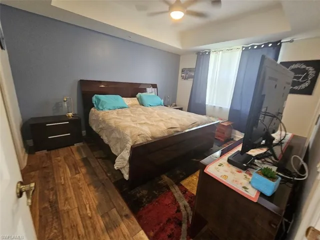 Bedroom featuring a tray ceiling, wood-type flooring, and ceiling fan