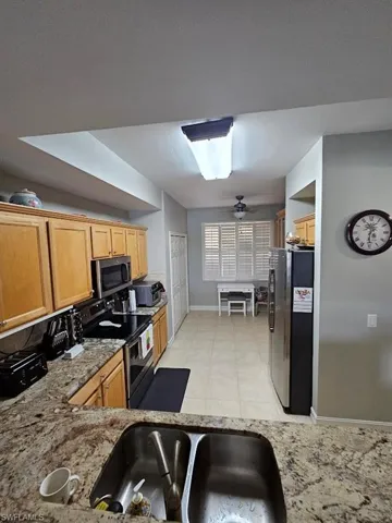 Kitchen featuring appliances with stainless steel finishes, light stone counters, light tile patterned floors, ceiling fan, and light brown cabinetry