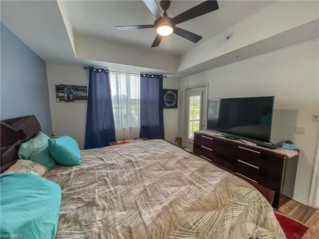 Bedroom with a raised ceiling, wood finished floors, and a ceiling fan