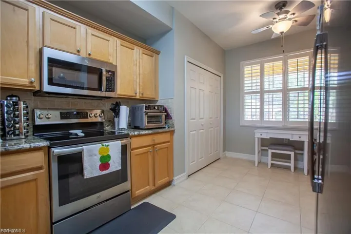 Kitchen with stainless steel appliances, backsplash, dark stone countertops, and light tile patterned flooring