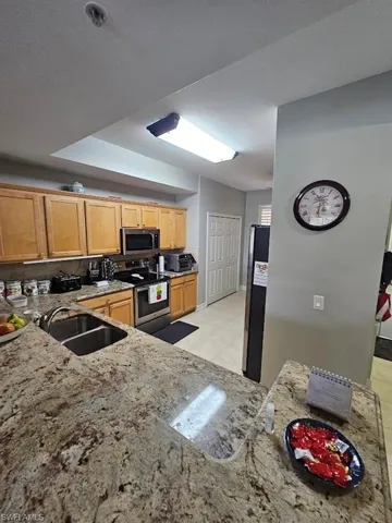 Kitchen with stainless steel appliances, light stone countertops, light tile patterned floors, and light brown cabinetry
