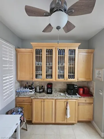 Kitchen with tasteful backsplash, light brown cabinets, glass insert cabinets, and light stone countertops