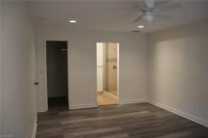 Unfurnished bedroom featuring a spacious closet, dark wood-style floors, ceiling fan, recessed lighting, and ensuite bathroom