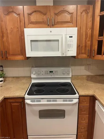 Kitchen with white appliances, brown cabinets, light countertops, and backsplash