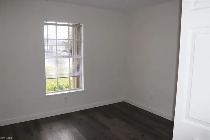 Empty room featuring baseboards and dark wood-style flooring