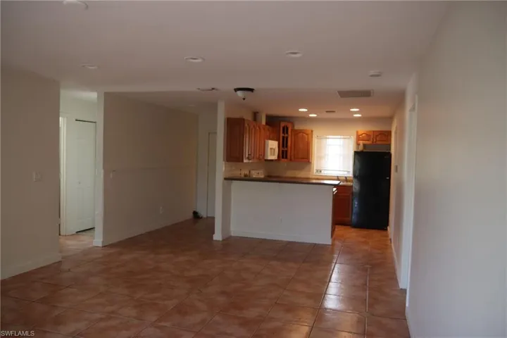 Kitchen featuring dark countertops, freestanding refrigerator, glass insert cabinets, brown cabinets, and recessed lighting