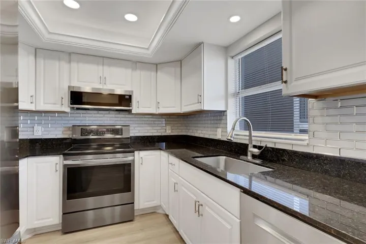 Updated Kitchen with Stainless Steel Appliances, White Cabinetry, Dark Stone Countertops and Light Wood Flooring