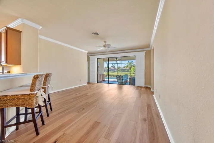 Living area featuring visible vents, a ceiling fan, ornamental molding, light wood-style floors, and baseboards