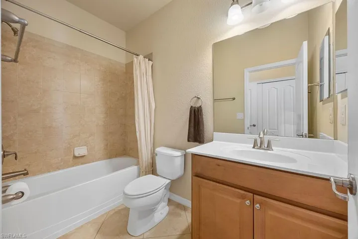 Full bath featuring tile patterned flooring, shower / bathtub combination with curtain, toilet, vanity, and baseboards