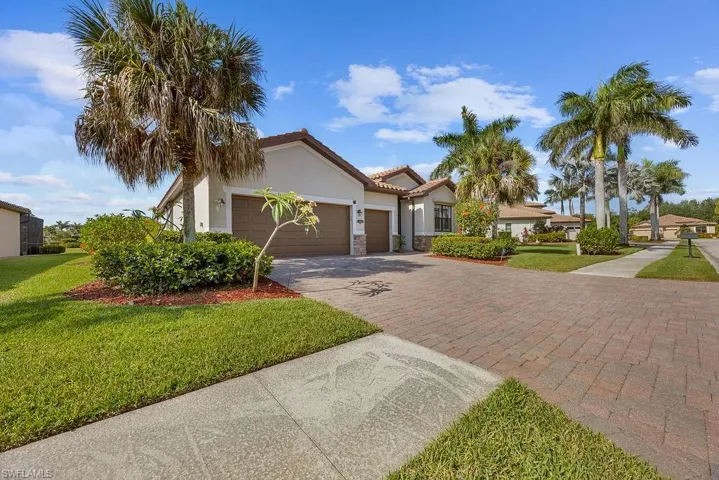 View of front facade featuring a tile roof, decorative driveway, a front lawn, an attached garage, and stucco siding