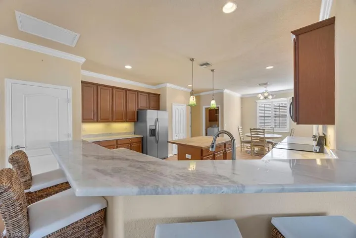 Kitchen with stainless steel refrigerator with ice dispenser, a breakfast bar, brown cabinets, and ornamental molding