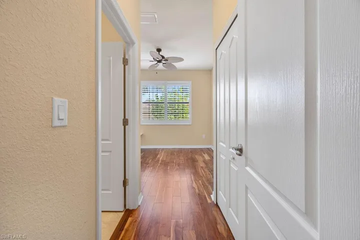 Hall featuring a textured wall, visible vents, baseboards, and wood finished floors