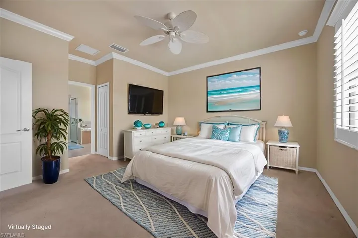 Carpeted bedroom with ornamental molding, multiple windows, connected bathroom, ceiling fan, and a closet