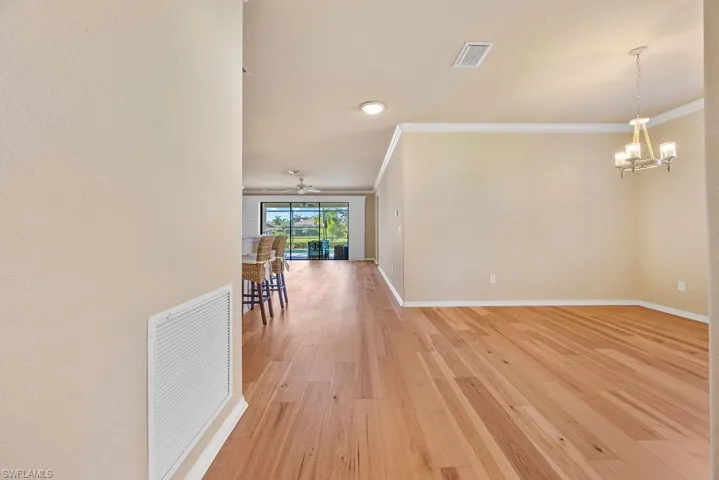 Hall featuring crown molding, light wood-style floors, an inviting chandelier, baseboards, and visible vents