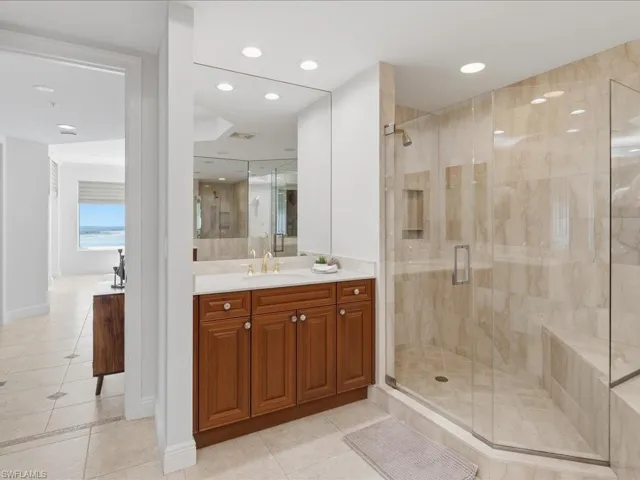 Spacious bathroom featuring a dual vanity with wood cabinetry and a large mirror, a glass-enclosed shower with a built-in bench, and recessed lighting