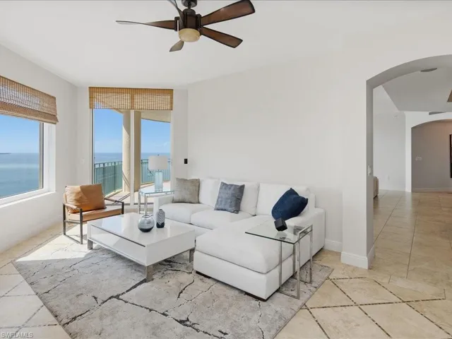 Spacious living area featuring large windows with natural light, a ceiling fan, and tile flooring with a decorative inlay