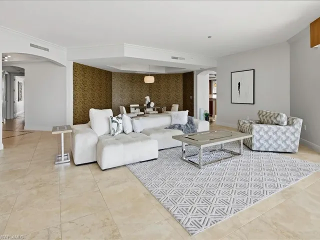 Spacious open-concept living area featuring light-toned tile flooring, crown molding, an arched entryway, and a dedicated dining space with distinctive wall covering