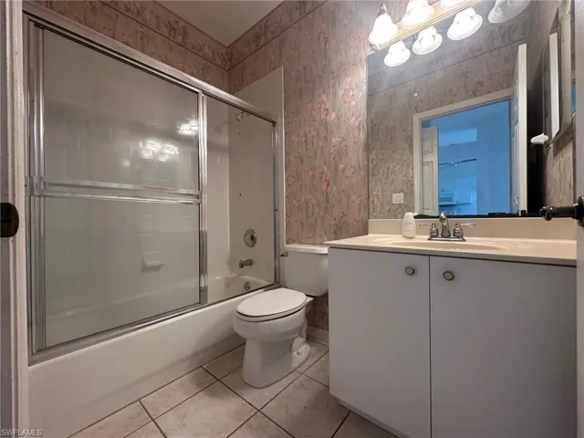 Full bathroom featuring toilet, wallpapered walls, enclosed tub / shower combo, and tile patterned floors