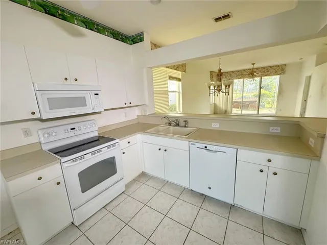 Kitchen with white appliances, sink, pendant lighting, light tile patterned floors, and white cabinetry