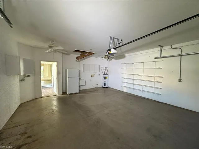 Garage with water heater, white fridge, and a garage door opener