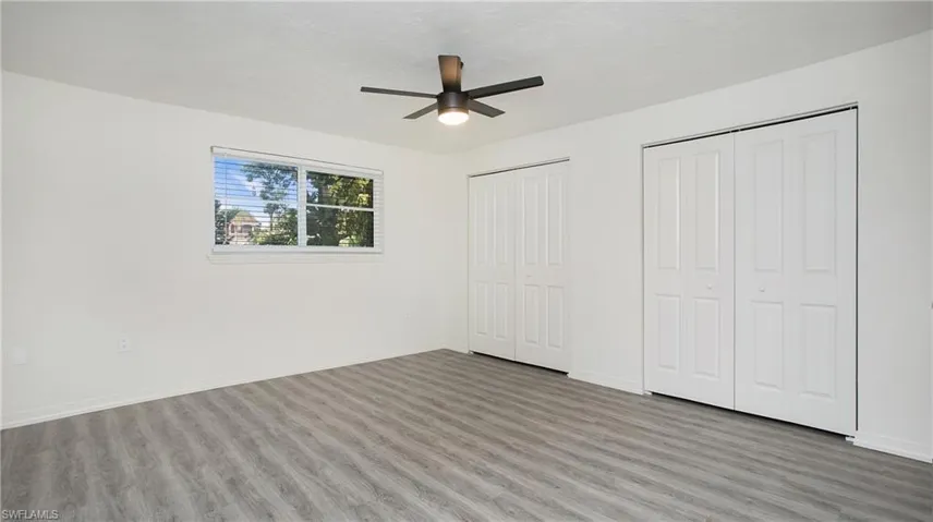 Unfurnished bedroom with two closets, wood finished floors, and a ceiling fan