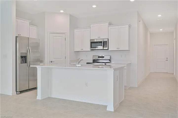 Kitchen featuring appliances with stainless steel finishes, white cabinets, light tile patterned floors, a kitchen island with sink, and sink